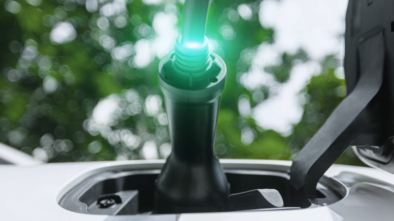 EV charger plug into electric car for electric recharge by electric charging station with glowing light cable, below tree closeup. Cutting-Edge innovation of green future energy sustainability Peruse